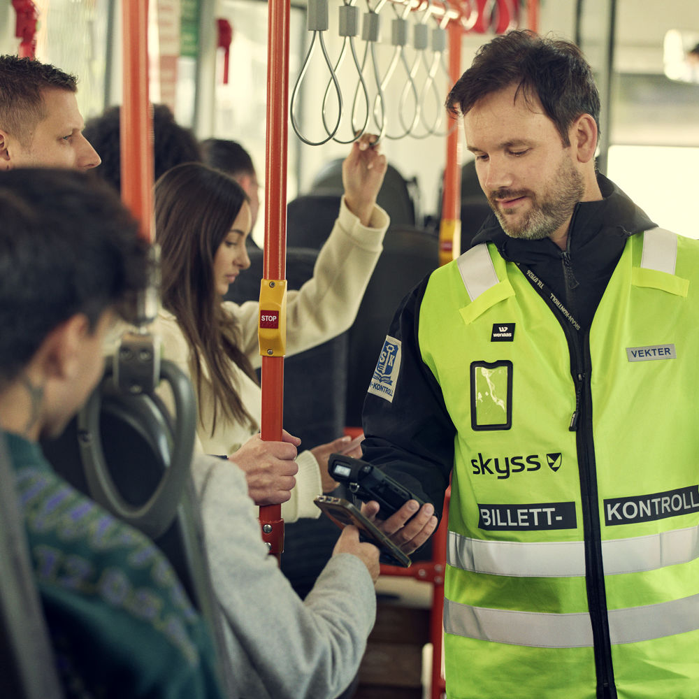 Bildet viser ein kontrollør som utfører billettkontroll om bord på ein buss.